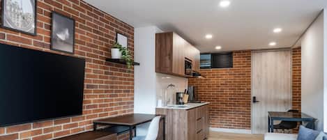 A compact living space with a kitchen, dining area, and a TV mounted on a brick wall.