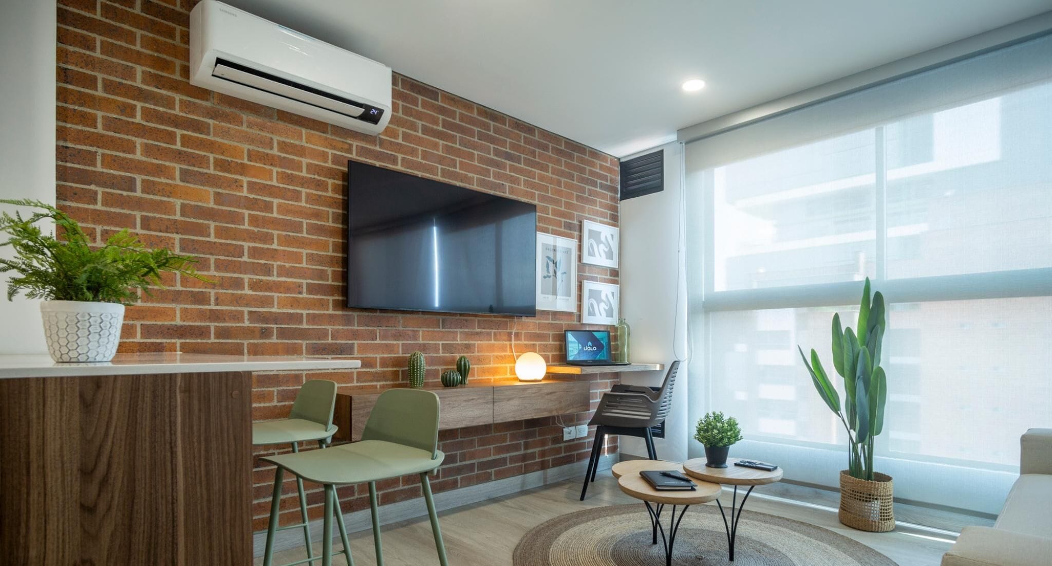 A modern living room with a brick wall, a flat-screen TV, a fireplace, and a large window.