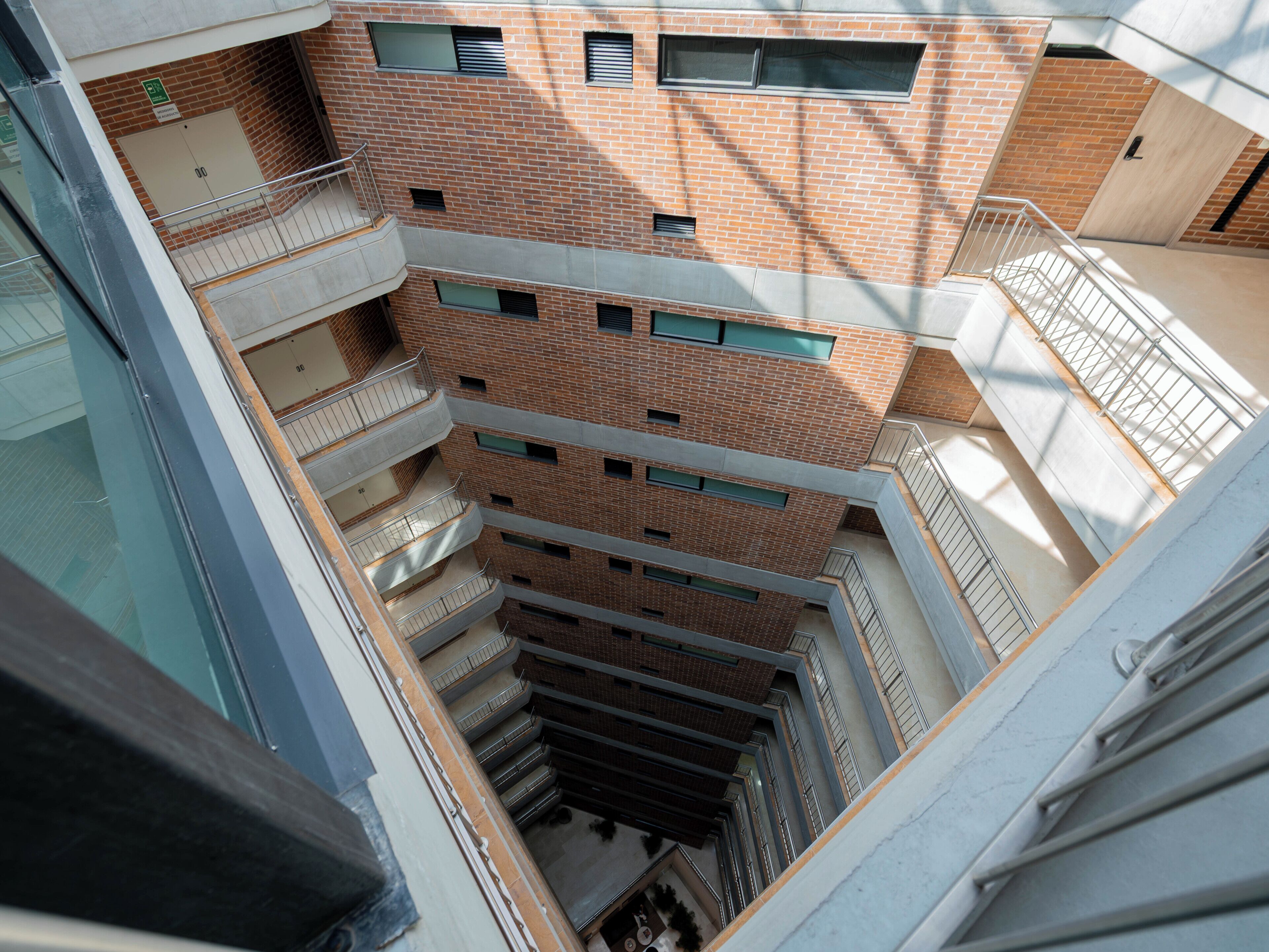 Un immeuble à plusieurs étages, doté d’une façade en briques, de nombreux balcons et d’un atrium central.