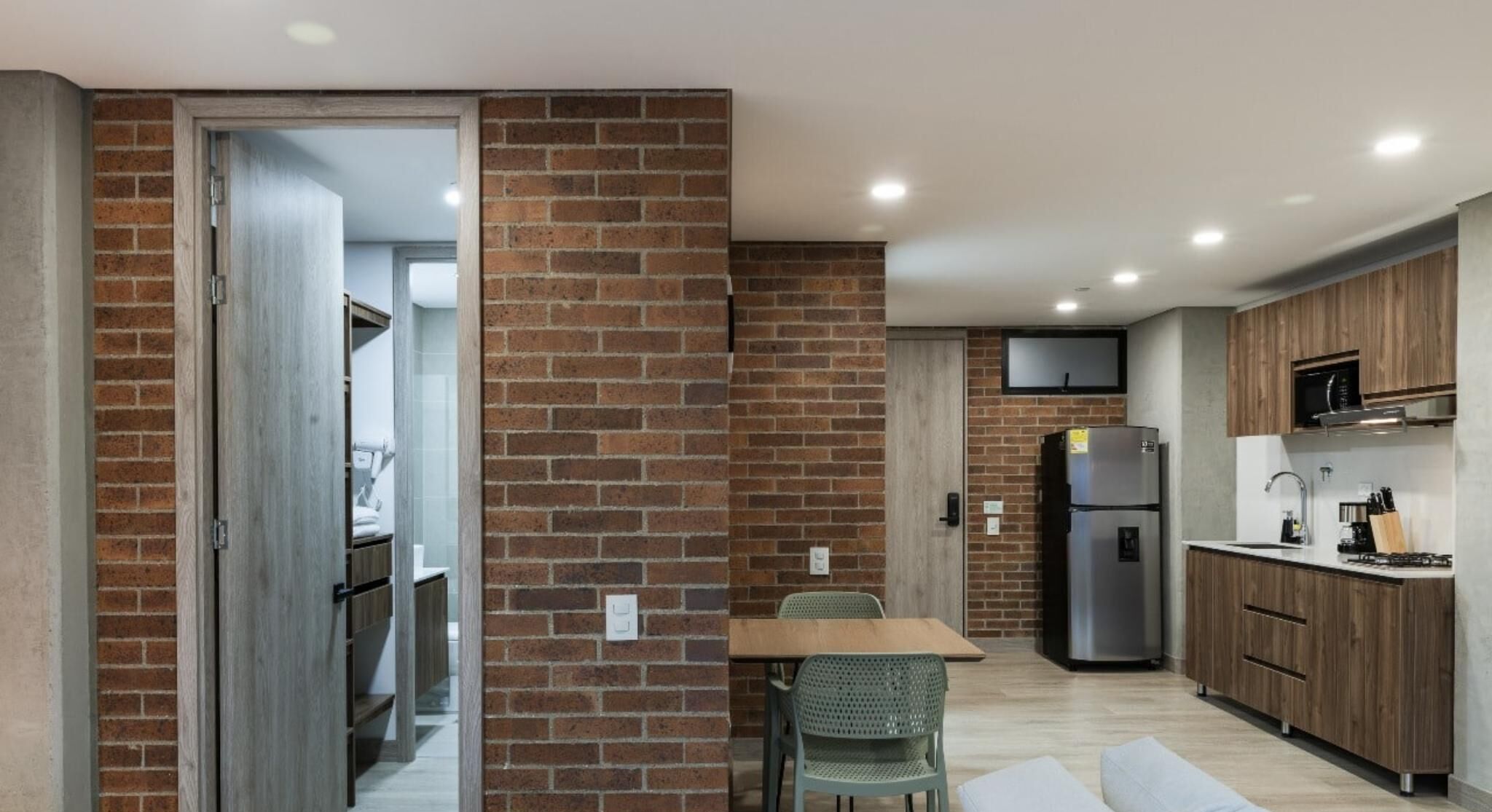 A modern kitchen with brick walls, a dining area with a table and chairs, and a refrigerator.