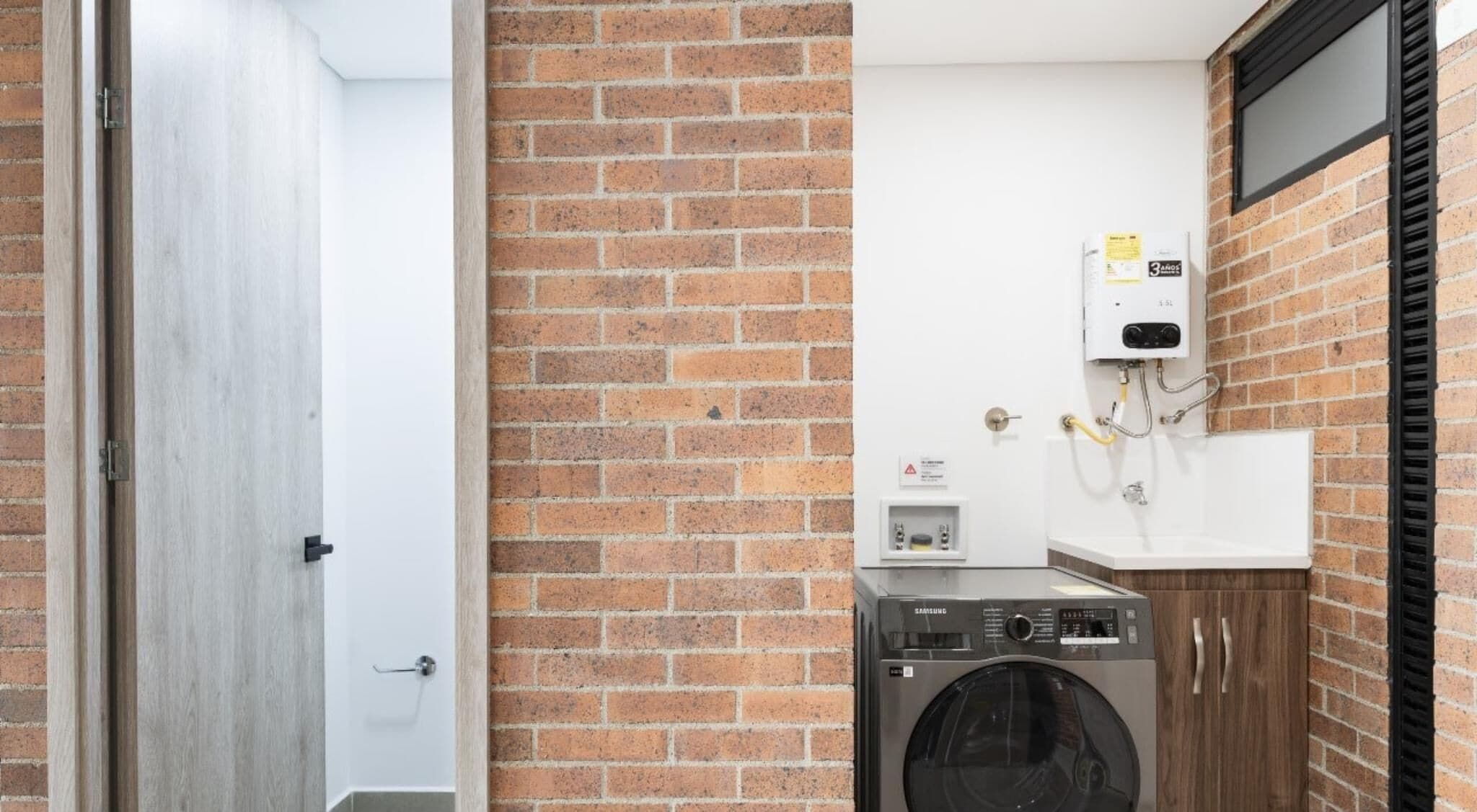 Een wasserette met een bakstenen muur, een wasmachine en een boiler.