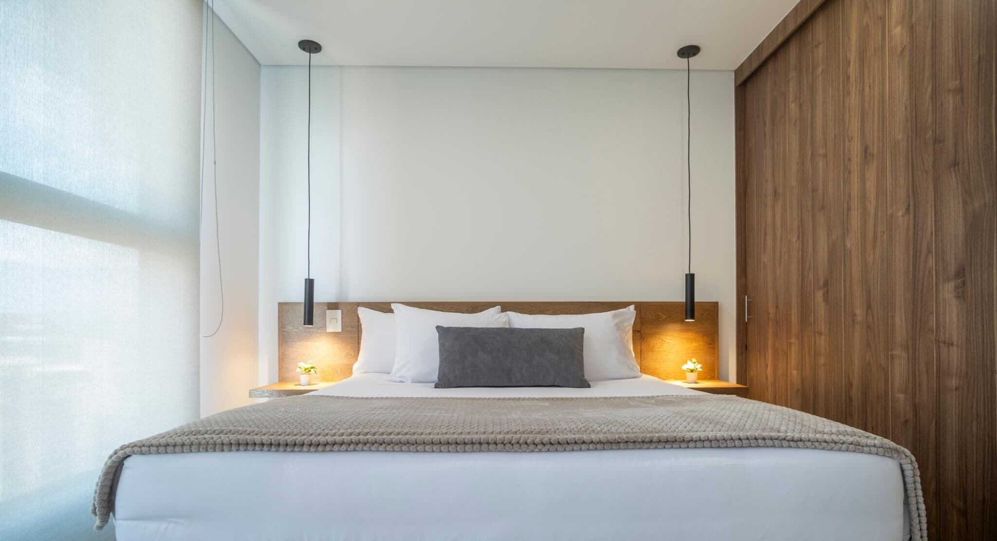 A modern hotel room with a large bed, wooden headboard, and two bedside lamps.