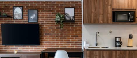 A modern kitchen with a brick wall, wooden cabinets, a flat-screen TV, a sink, and a coffee machine.