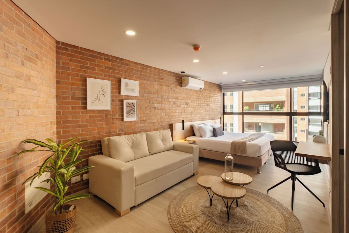 A modern living room with a brick wall, a sofa, a bed, a dining table, and a potted plant.