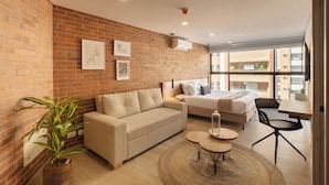 A modern living room with a brick wall, a sofa, a bed, a dining table, and a potted plant. - Kyux by Jalo (Medellín)