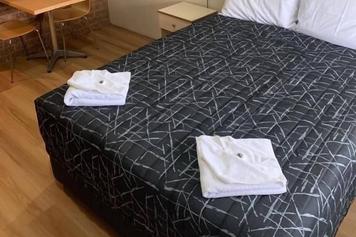 Ett hotellrum med en stor säng, ett skrivbord, en stol, ett nattduksbord och en lampa.