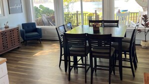 Un espace repas avec une table et des chaises en bois, de grandes fenêtres donnant sur un lac et un plafond avec des poutres apparentes.