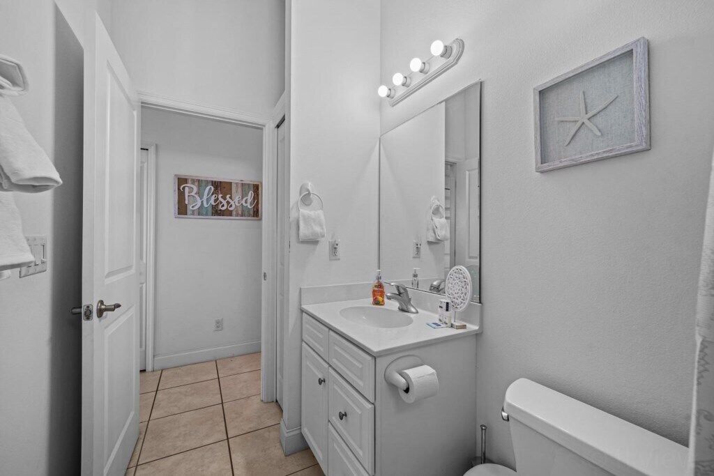 A bathroom with a white vanity, a toilet, a mirror with lights, and a towel rack.