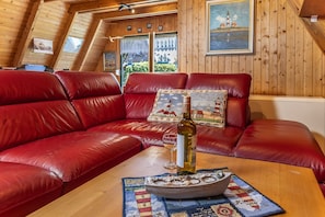 Un canapé en cuir rouge, une bouteille de vin et un verre posés sur une table en bois, le tout agrémenté d’un coussin aux motifs marins.