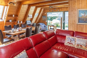 Una stanza accogliente con un divano in pelle rossa, pareti in legno, un tavolo da pranzo con sedie e un computer sul tavolo.
