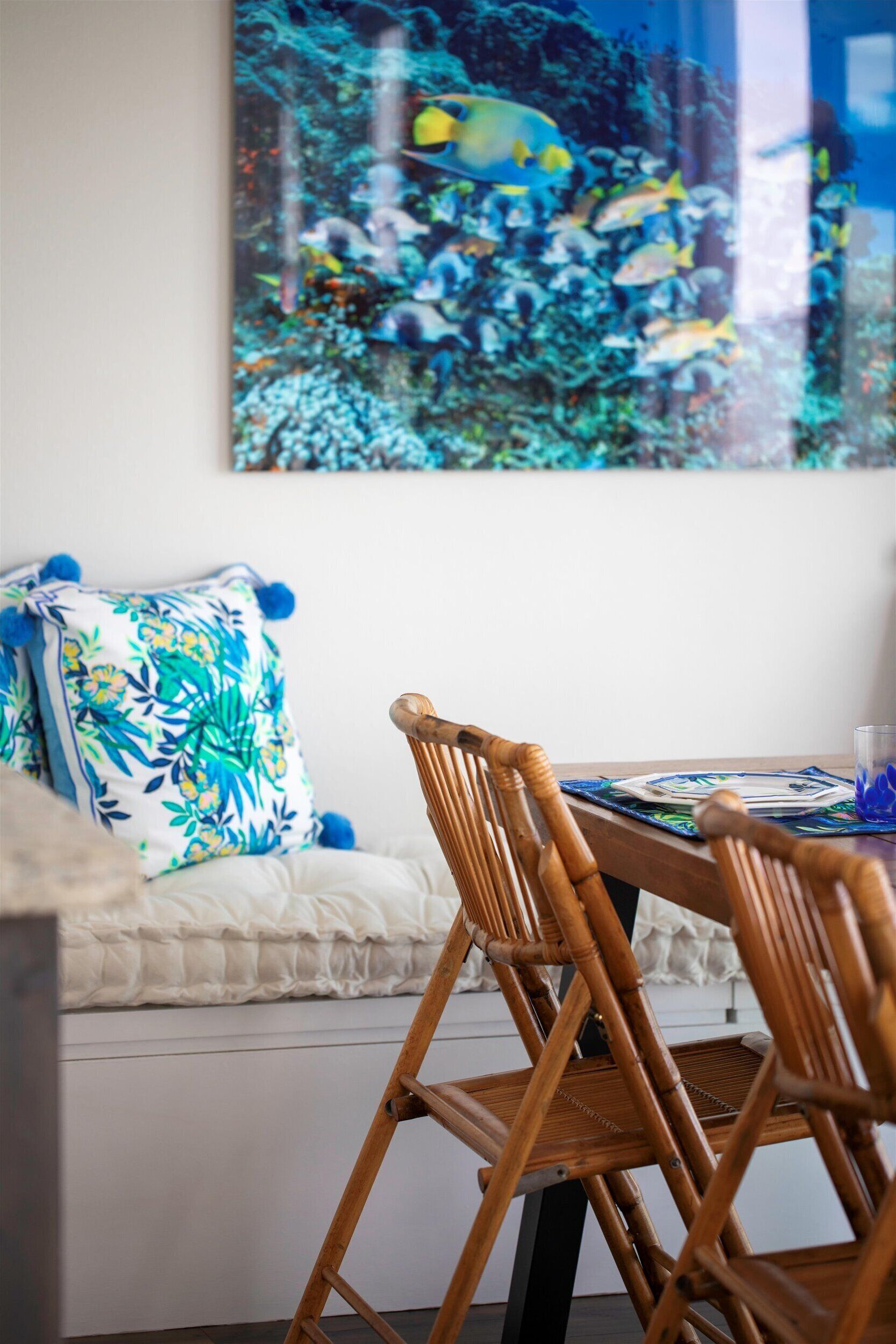 A dining area with a wooden table, a woven chair, and a colorful pillow.