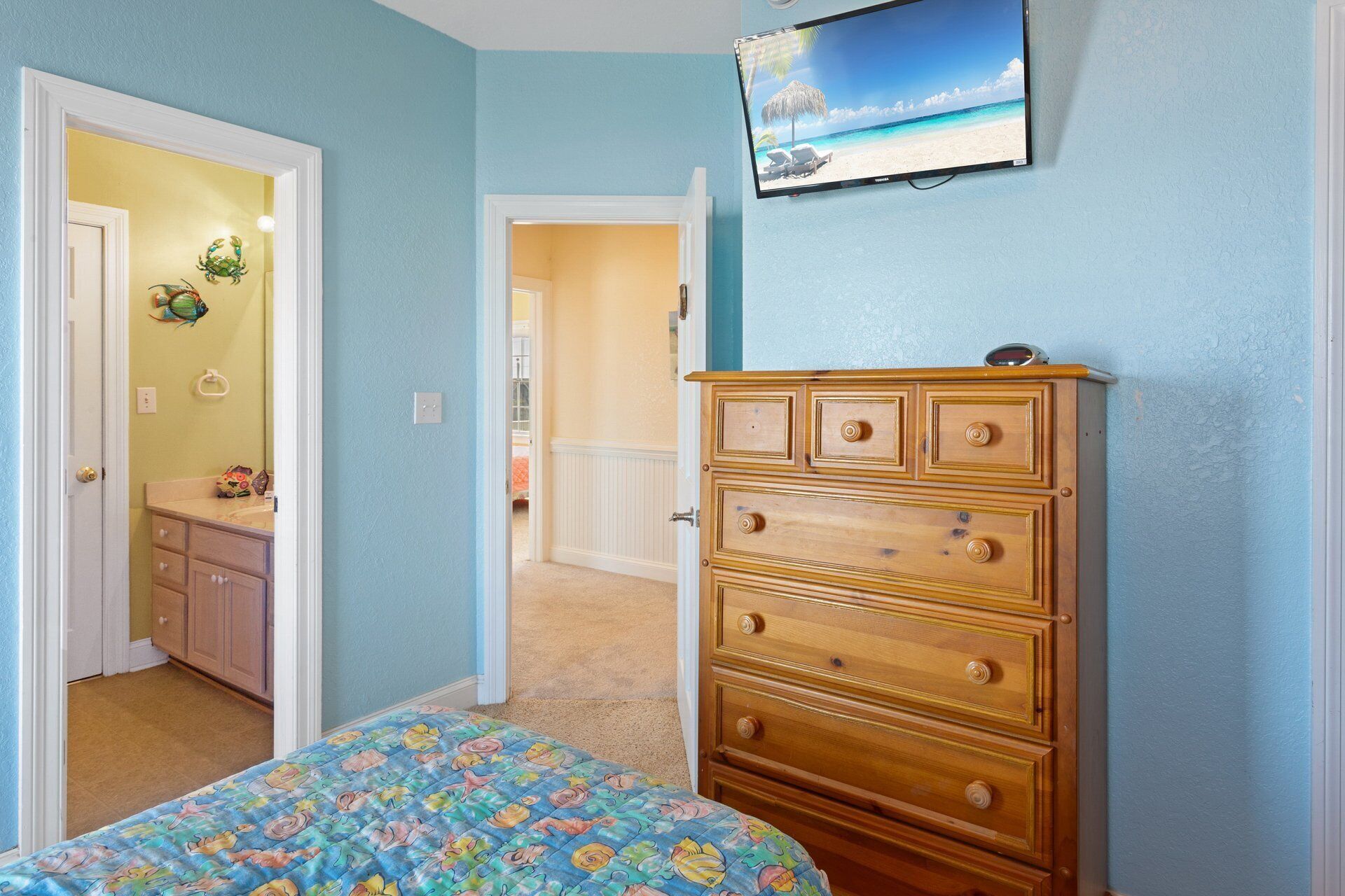 A bedroom with a bed, dresser, and TV displaying a beach scene.