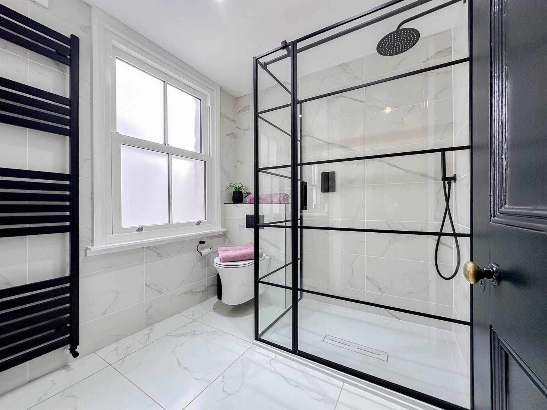 Ein Badezimmer mit Duschkabine, Toilette, Fenster und Handtuchhalter.
