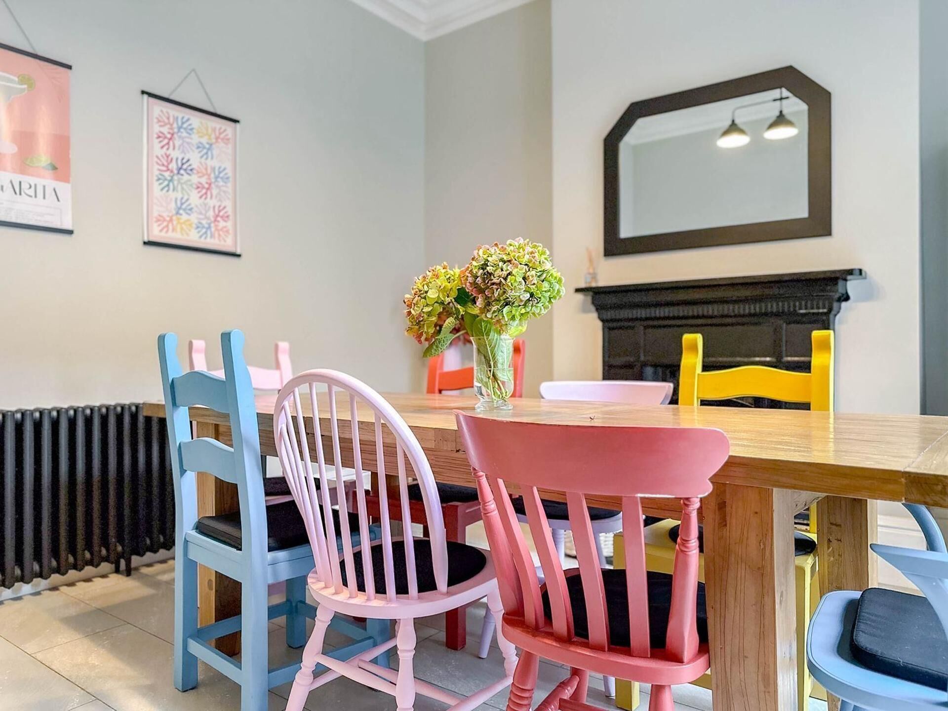 A dining area with a wooden table, two chairs, a vase with flowers, and a fireplace.