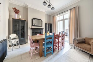 Een eetruimte met een houten tafel en stoelen, een zwart kastje en een grote spiegel boven de tafel.