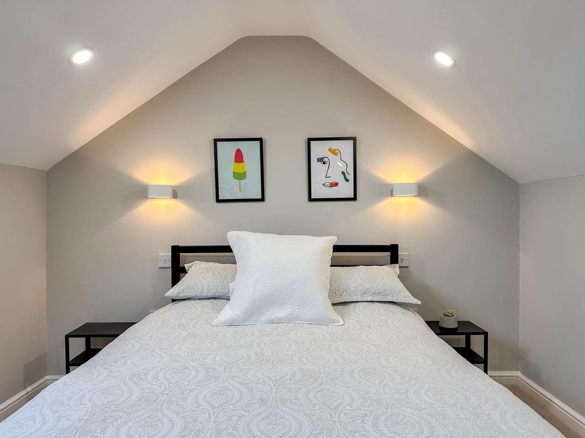 A bedroom with a bed, two wall-mounted light fixtures, and two framed artworks.