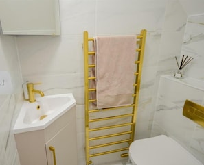 Une salle de bain avec un lavabo blanc, un robinet doré, des toilettes blanches et un porte-serviettes avec une serviette rose.