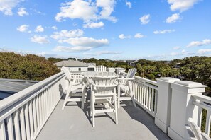 Un espace extérieur abrité, doté de chaises Adirondack blanches et d’une balustrade blanche.