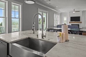 Une cuisine moderne dotée d’un grand îlot central, d’appareils électroménagers en acier inoxydable et offrant une vue sur l’extérieur.