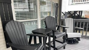 Een houten terras met buitenmeubilair, waaronder twee Adirondack-stoelen en een kleine tafel.