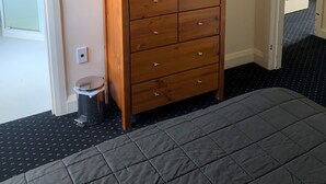 Een kamer met een houten dressoir, een aan de muur bevestigde televisie, een kleine prullenbak en een deur naar een andere kamer.