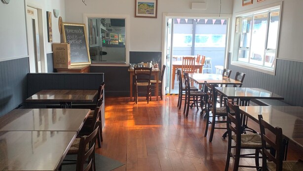 Een restaurant met houten tafels en stoelen, een balie met een krijtbordmenu en uitzicht door het raam.
