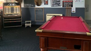 Een biljartruimte met een pooltafel, een jukebox en gevulde hertenkoppen aan de muur.