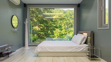 Un dormitorio con un ventanal grande, una cama, una mesita de noche y una lámpara moderna.