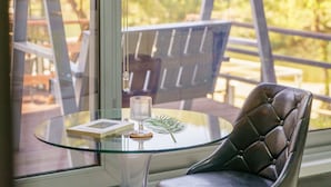 Una mesa de vidrio con un libro, un vaso y una hoja decorativa. Una silla de cuero está ubicada frente a la mesa.