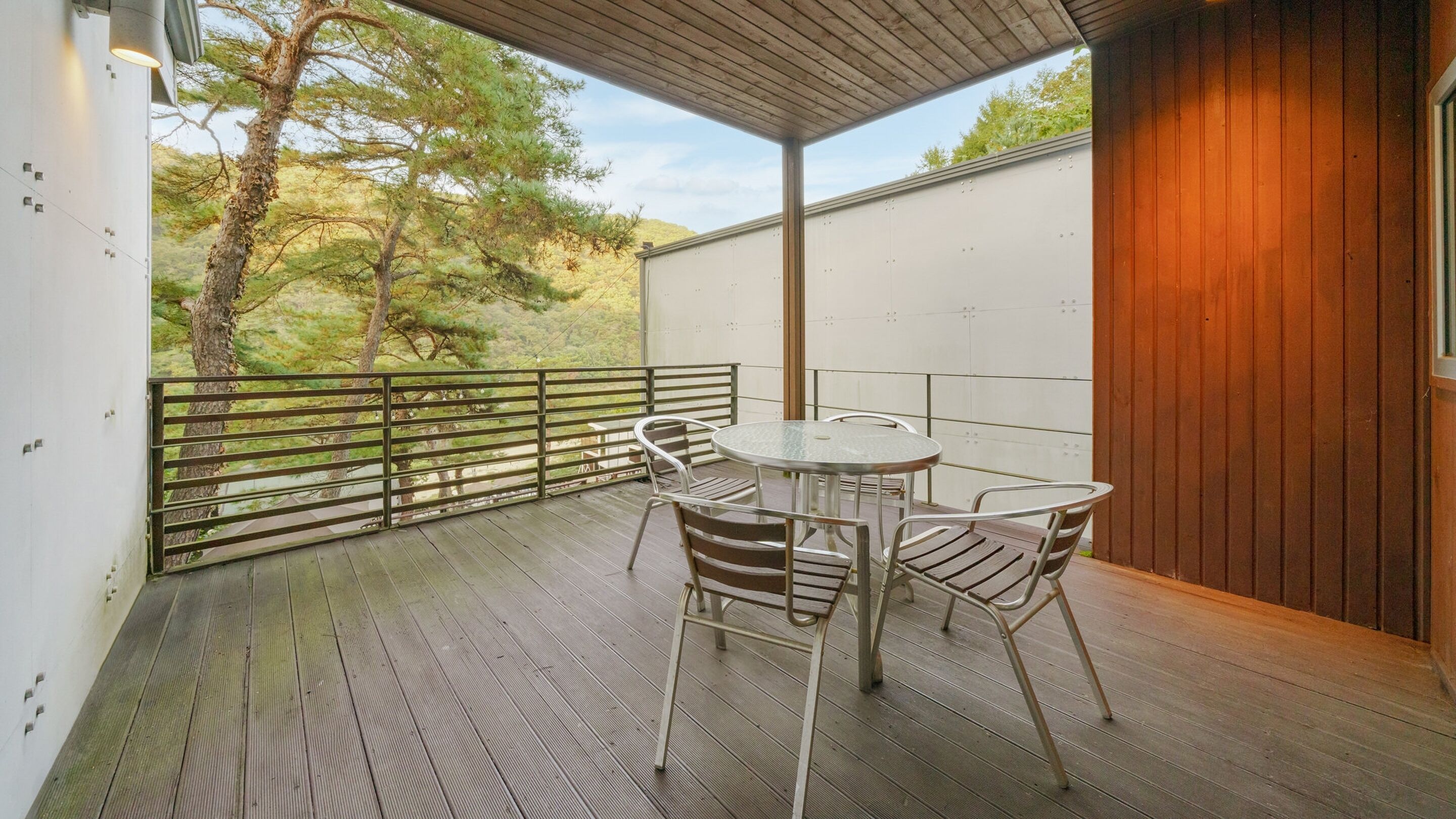 Uma varanda com mesa e cadeiras, com vista para uma paisagem natural com árvores e uma colina.