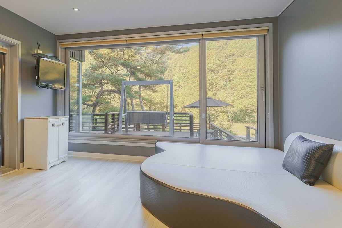 A modern room with a large sliding glass door leading to an outdoor deck, a built-in bench, and a flat-screen TV mounted on the wall.