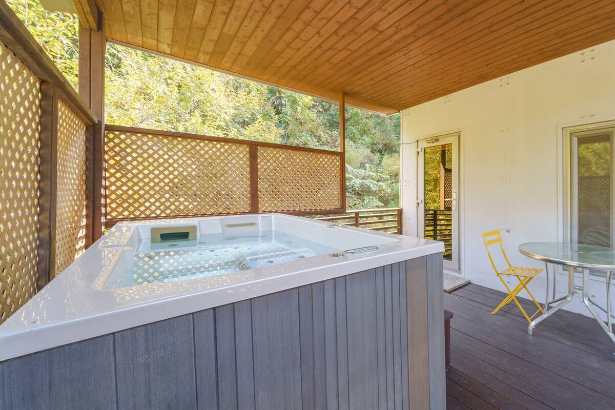 A hot tub area with a wooden deck, a glass table, and a yellow folding chair.