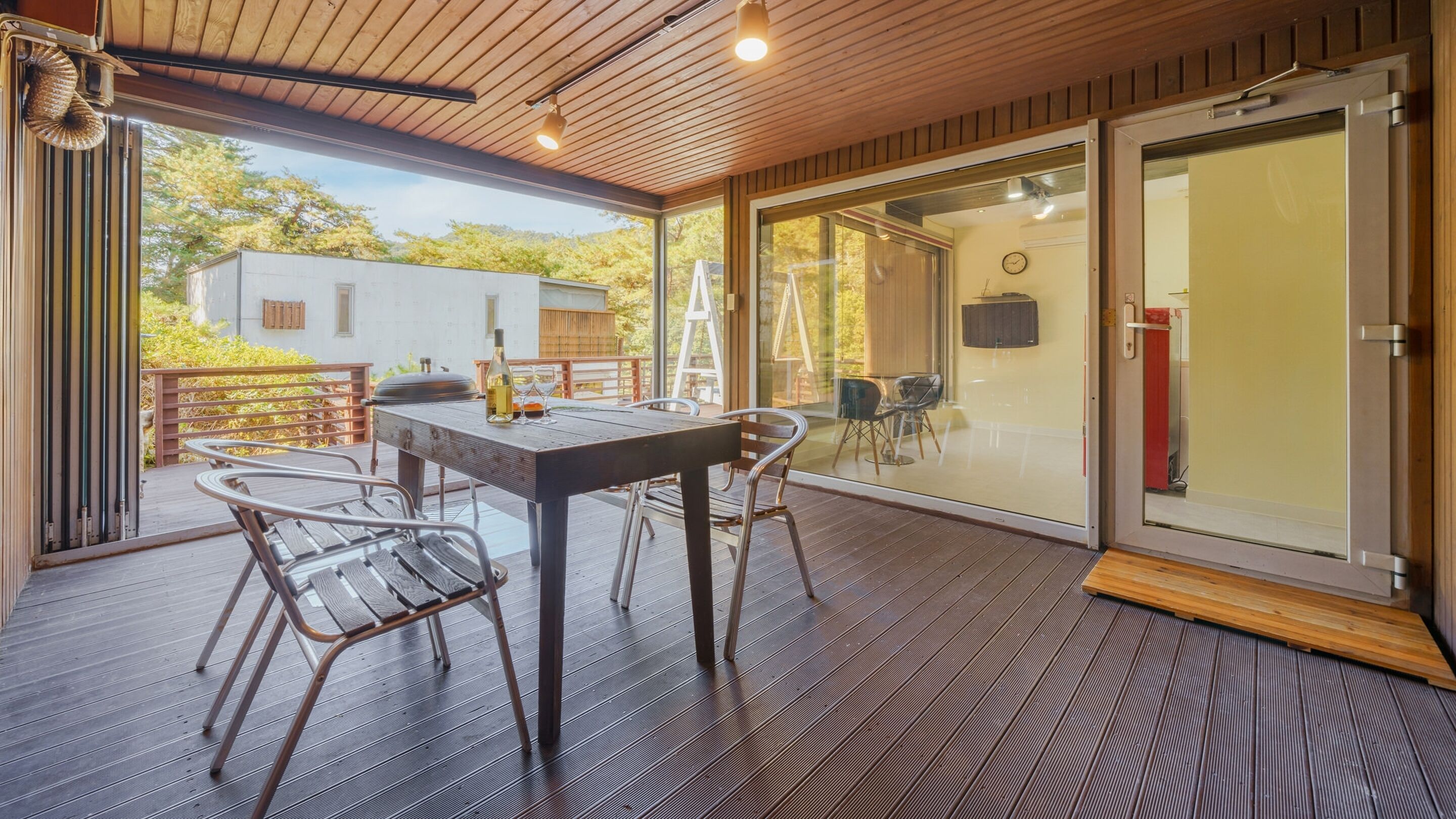 Un patio techado al aire libre con mesa y sillas, una terraza de madera y un ventanal corredero que da a un espacio interior.
