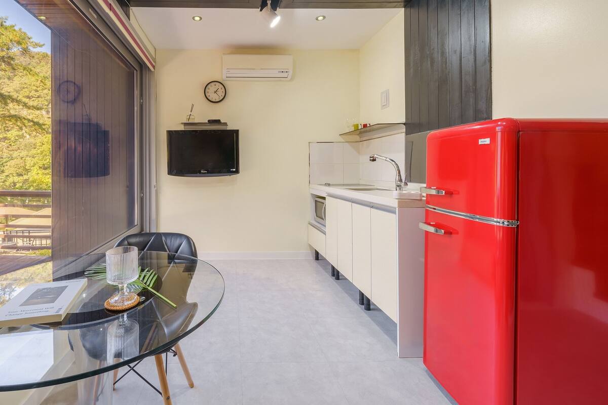 A compact kitchen with a red refrigerator, a glass table with a menu, and a view of the outdoors.