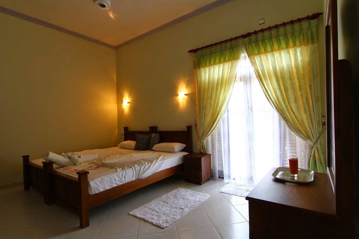 A neatly made bed with pillows, a bedside table with a glass of water, and a window with curtains.