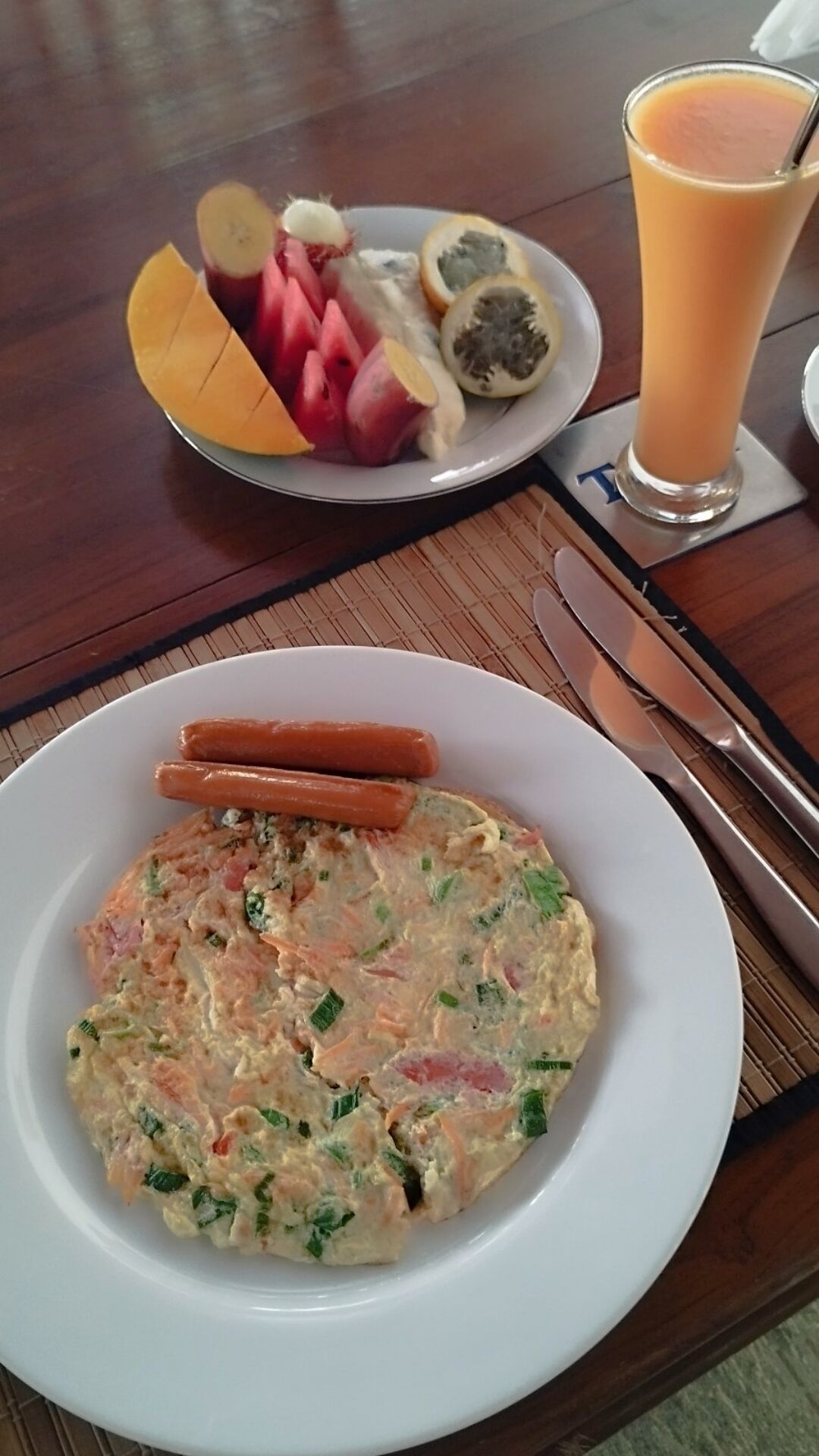 A plate of food with a salad, two sausages, and a glass of orange juice on a wooden table.