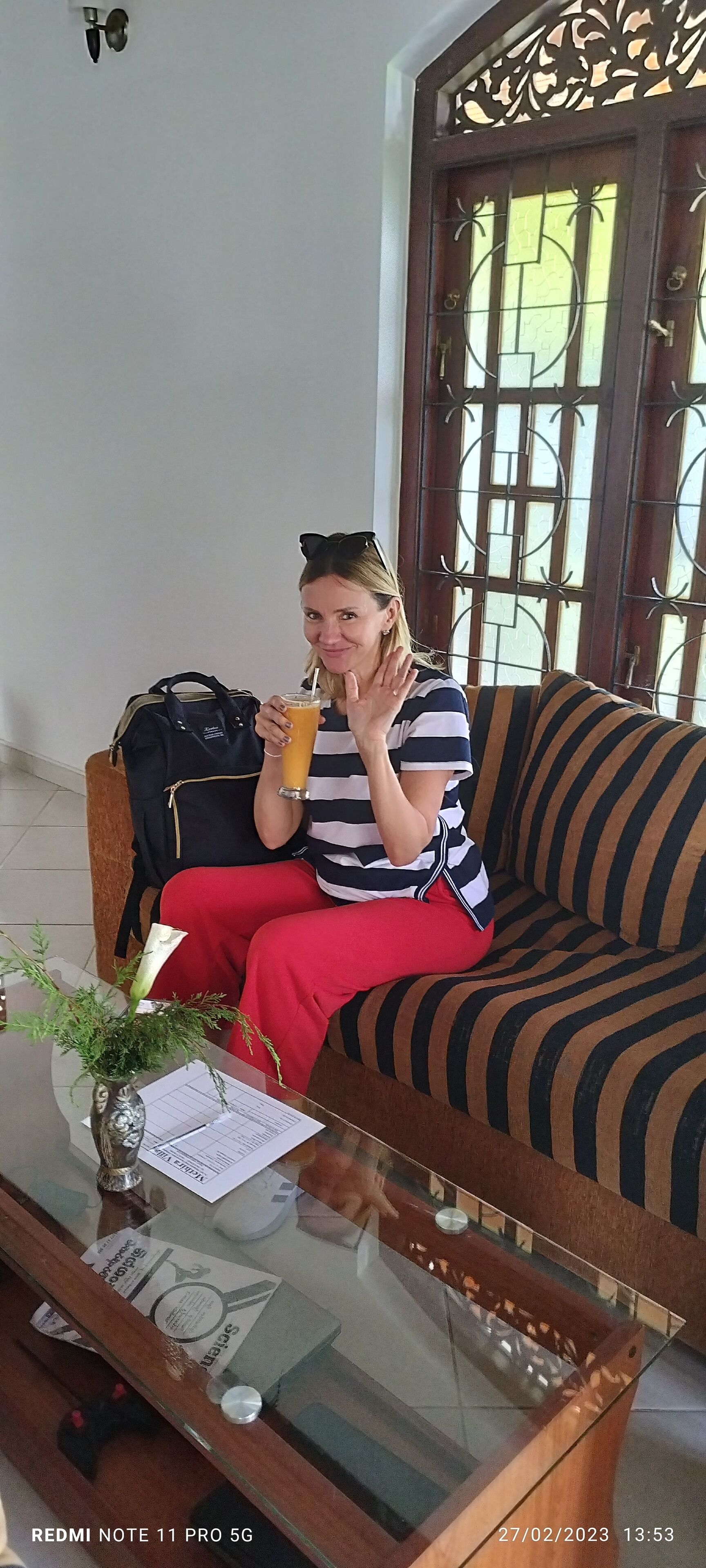 Una persona sentada en un sofá a rayas con una mesa de vidrio al frente, sosteniendo una bebida.