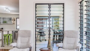 A modern living room with two grey armchairs, a wooden coffee table, and a glass partition with a view of the outside. - Beachside Escape by Cottonwood (Casuarina)