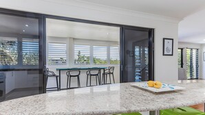 A kitchen with a marble countertop, green stools, and a dining area with a table and chairs. - Beachside Escape by Cottonwood (Casuarina)