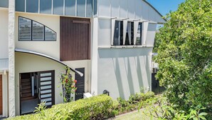 A modern two-story house with a curved roof, a wooden door, and a small garden area with various plants. - Beachside Escape by Cottonwood (Casuarina)