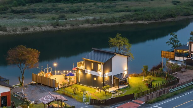 A modern house with a large deck overlooking a river, surrounded by a well-maintained garden.