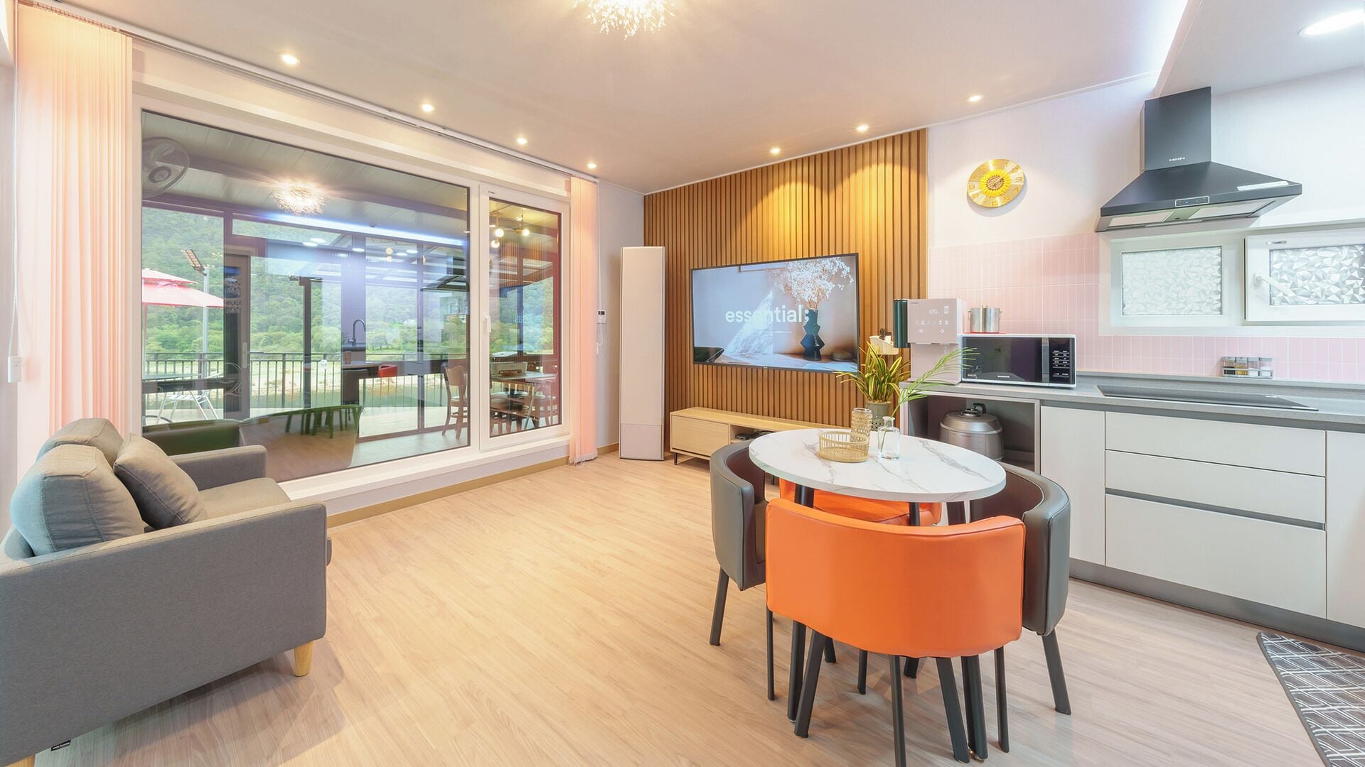 Una sala de estar moderna con sofá, mesa de comedor y sillas, una zona de cocina con microondas y un televisor en la pared.