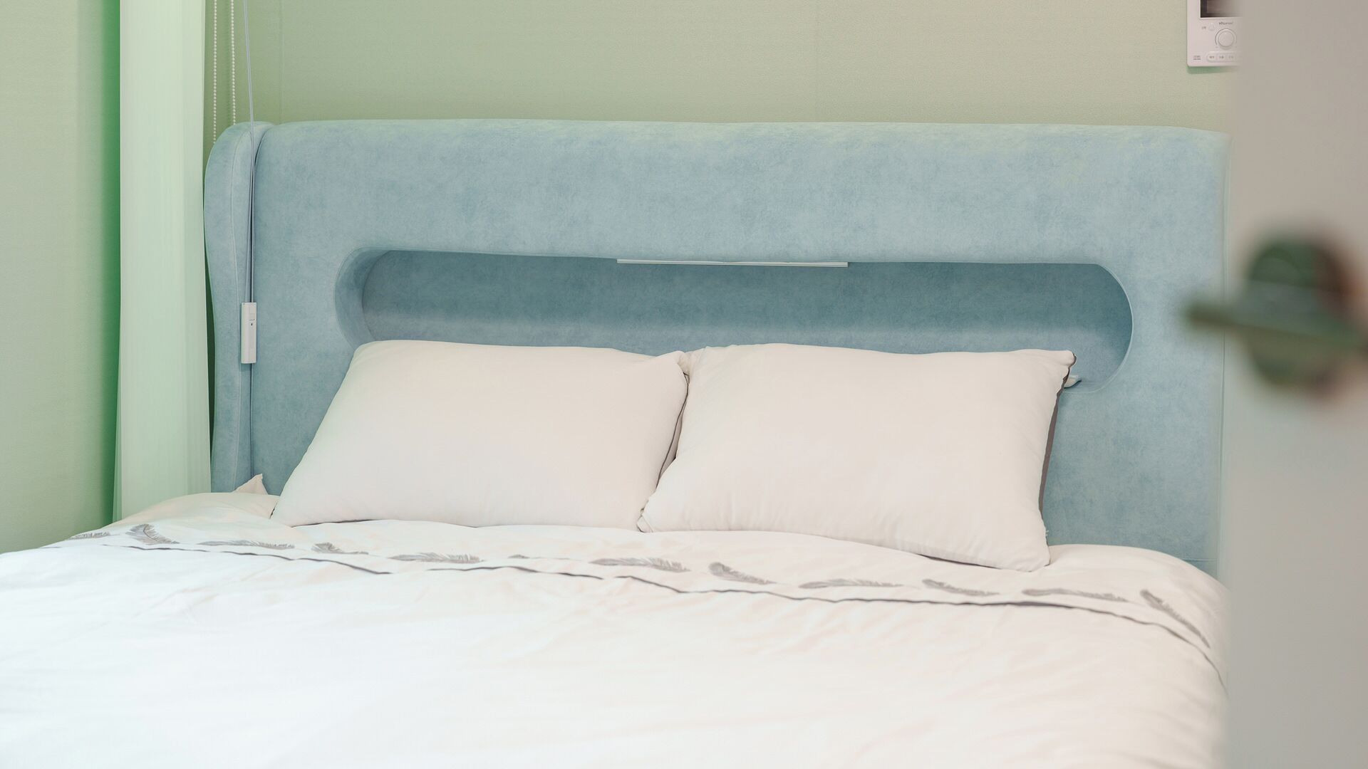 A bed with a light blue headboard, white pillows, and a white bedspread.