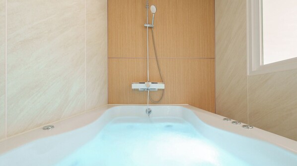 A modern bathroom with a freestanding bathtub, a handheld showerhead, and a wall-mounted control panel.