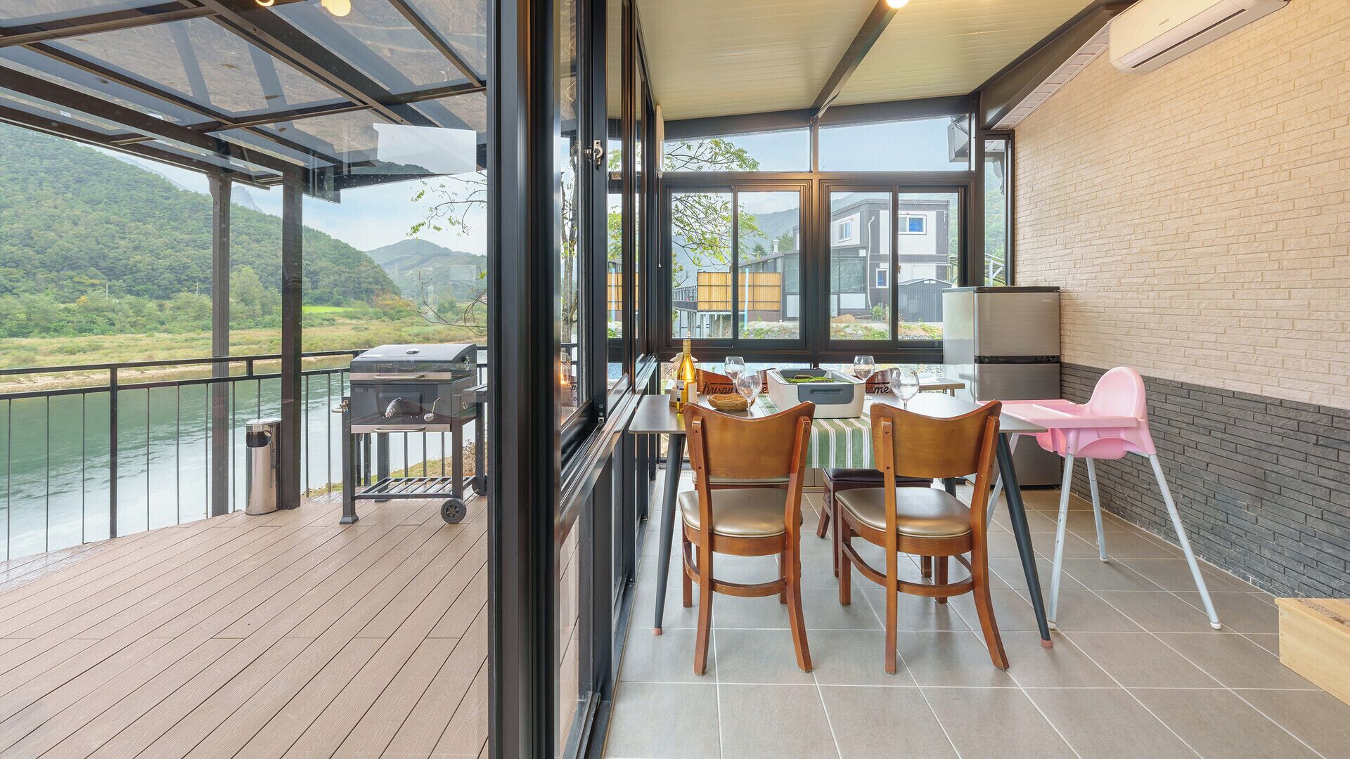 Un balcón con vistas a un río y montañas, una parrilla y una mesa con sillas.