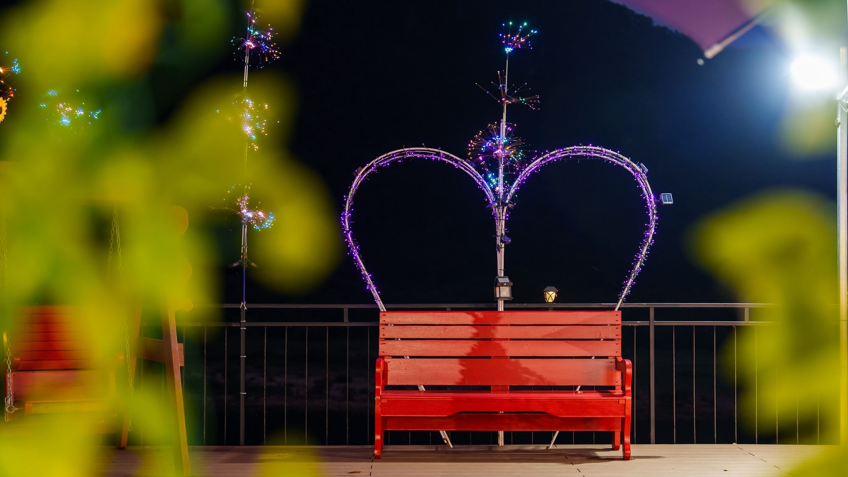 Un banco rojo con decoraciones luminosas en forma de corazón al fondo.