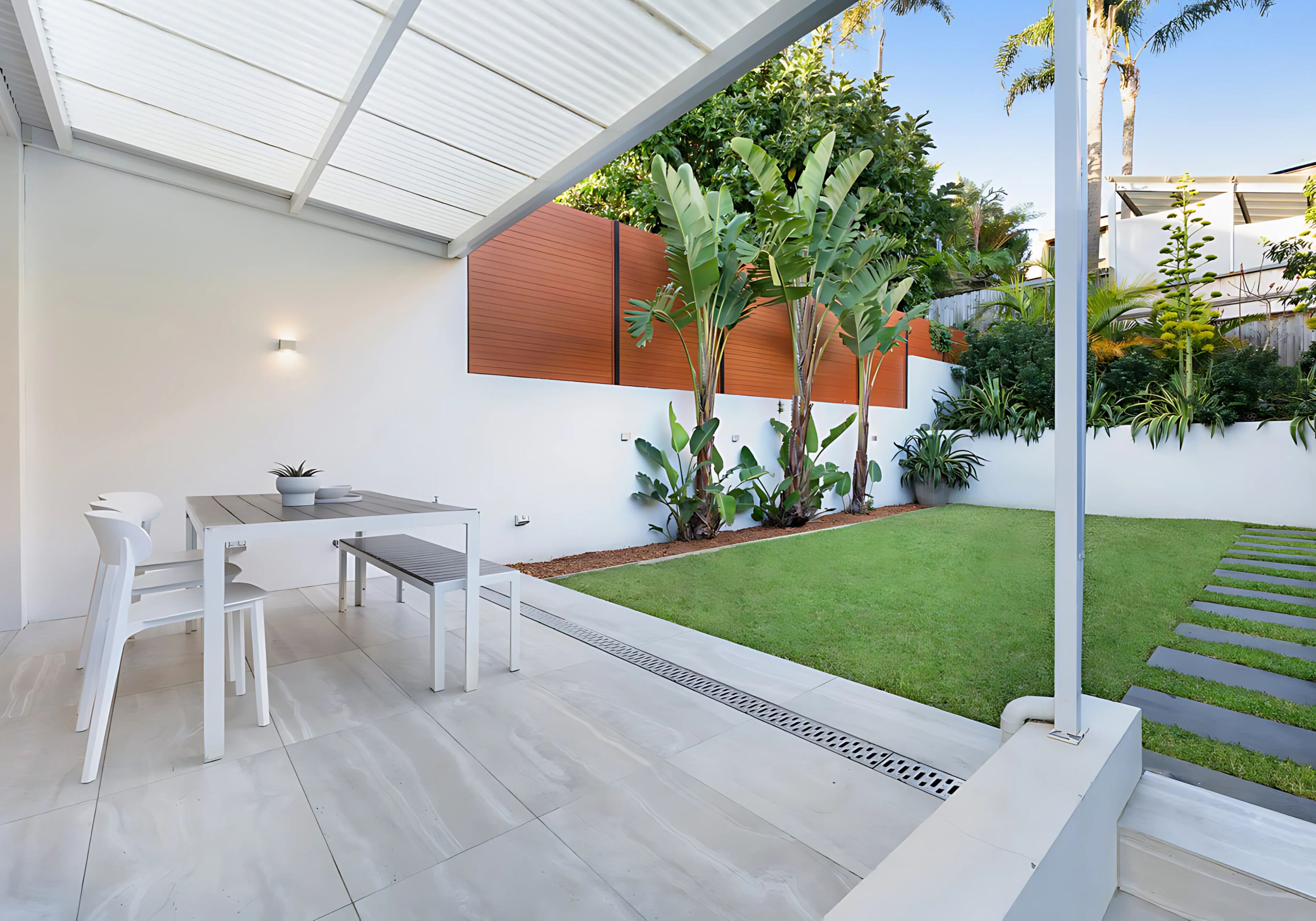 A modern patio with a white table and chairs, a small garden with tropical plants, and a clear view of the surrounding area.
