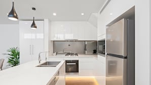 Una cocina moderna con armarios blancos, electrodomésticos de acero inoxidable e iluminación colgante.