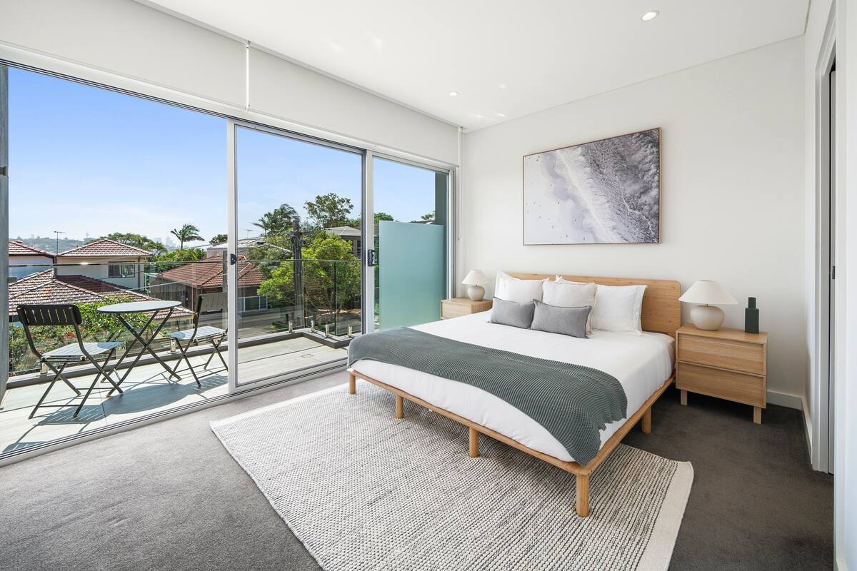 Un dormitorio moderno con una cama grande, una mesita de noche, una lámpara y vistas al exterior a través de una puerta corrediza de vidrio.