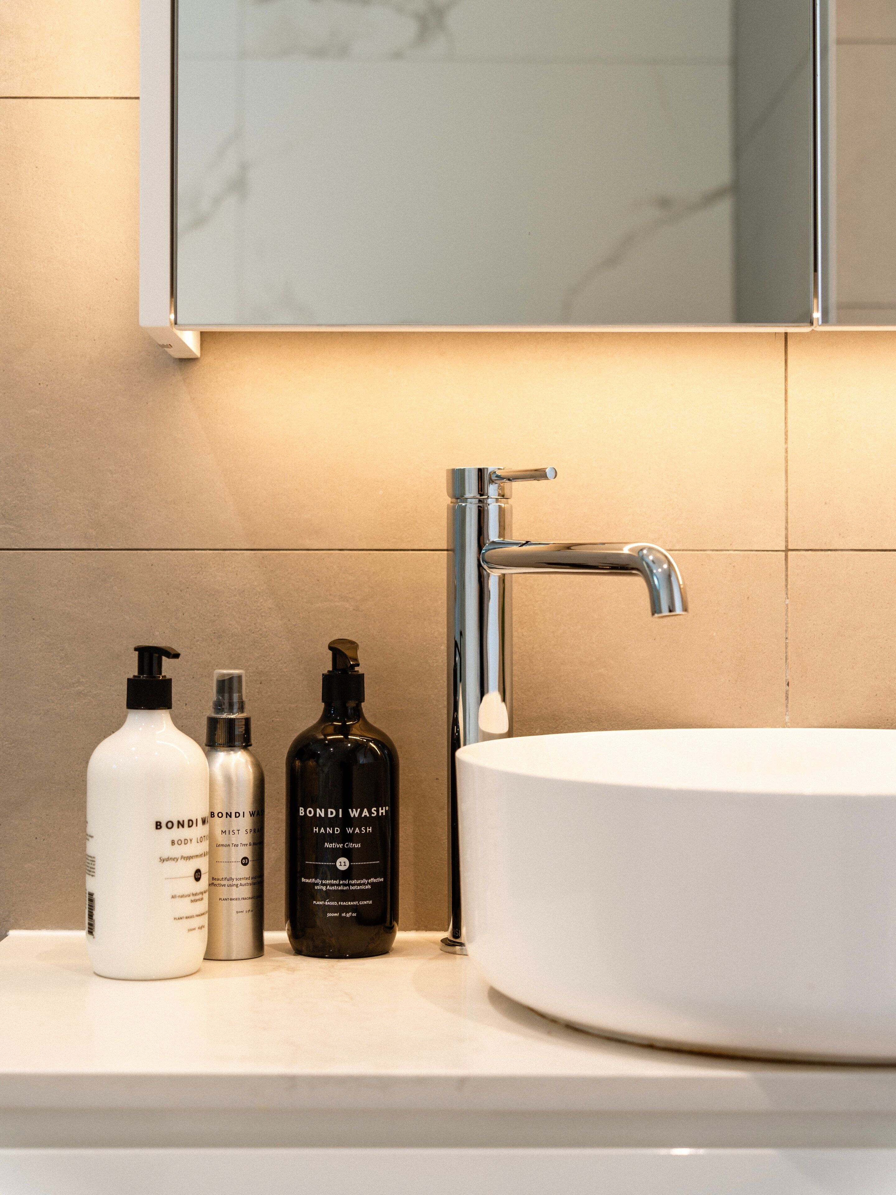 A bathroom sink with a chrome faucet and three bottles of hand wash soap on the countertop.